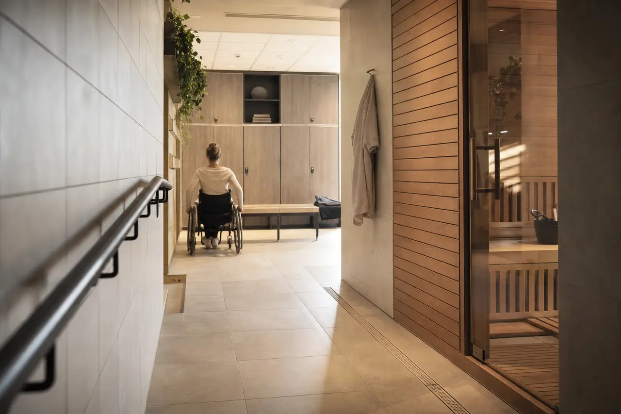 A wide tiled corridor with a handrail leading to a changing area in soft light