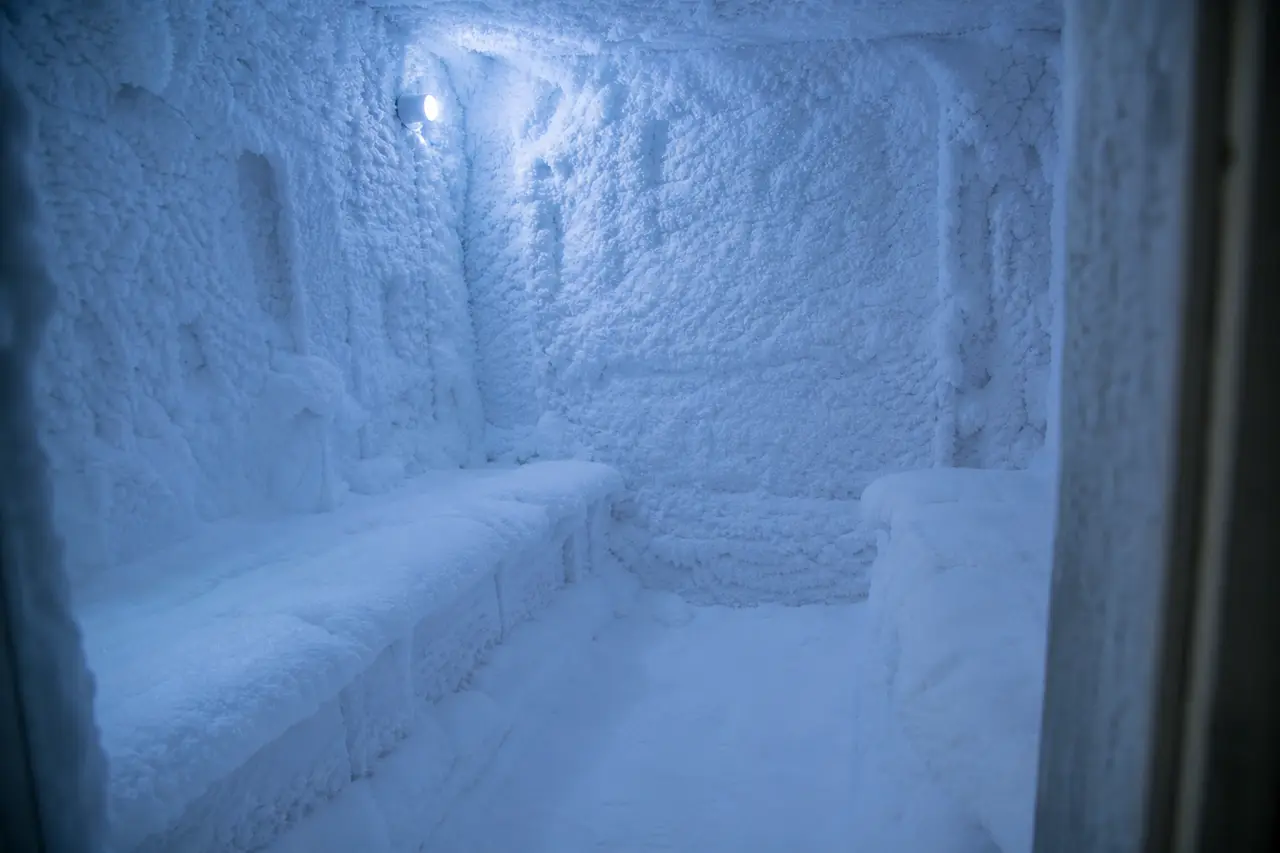 A small refrigerated room with snow-covered benches and walls lit by cool blue light