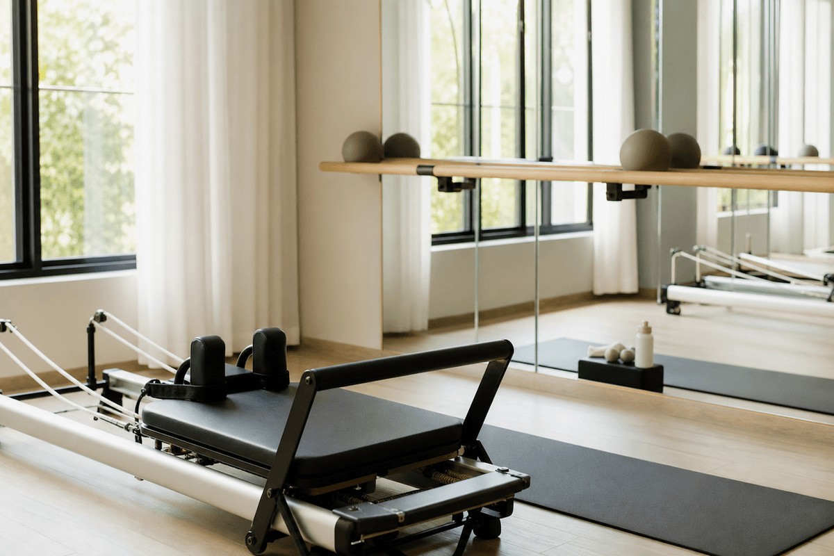 A studio with a Pilates reformer machine on one side and a ballet barre along the mirrored wall
