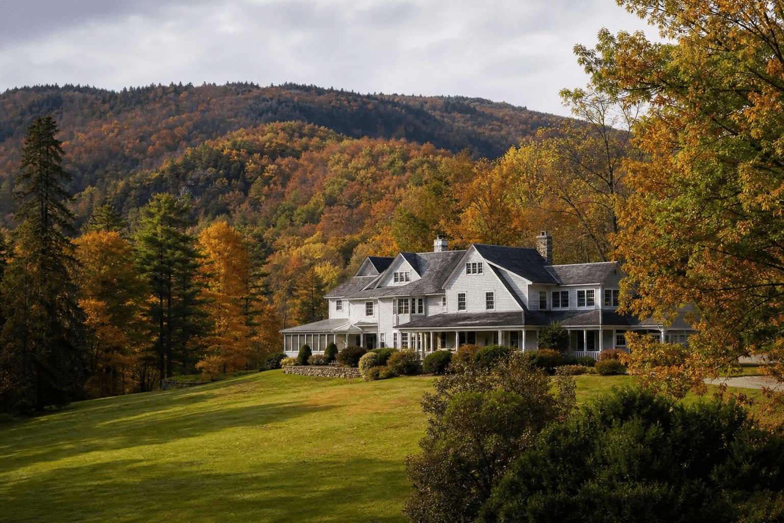 A classic New England retreat house among rolling wooded Berkshire hills in soft autumn light