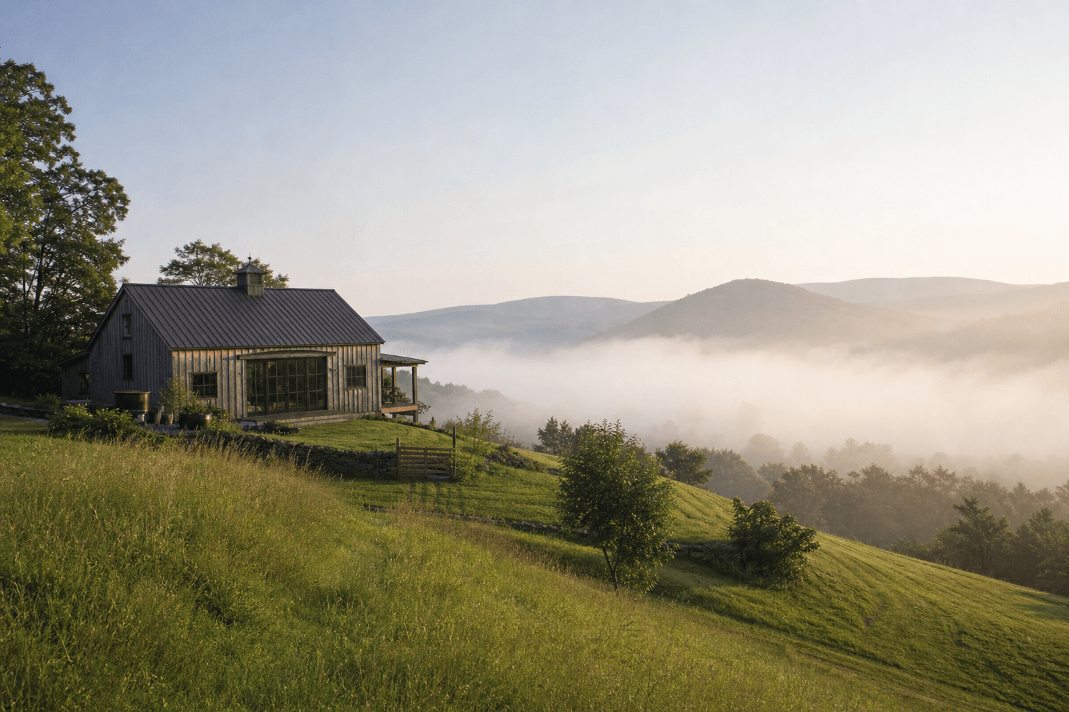 A converted barn retreat on a green hillside in the Catskills with morning mist rising off the valley
