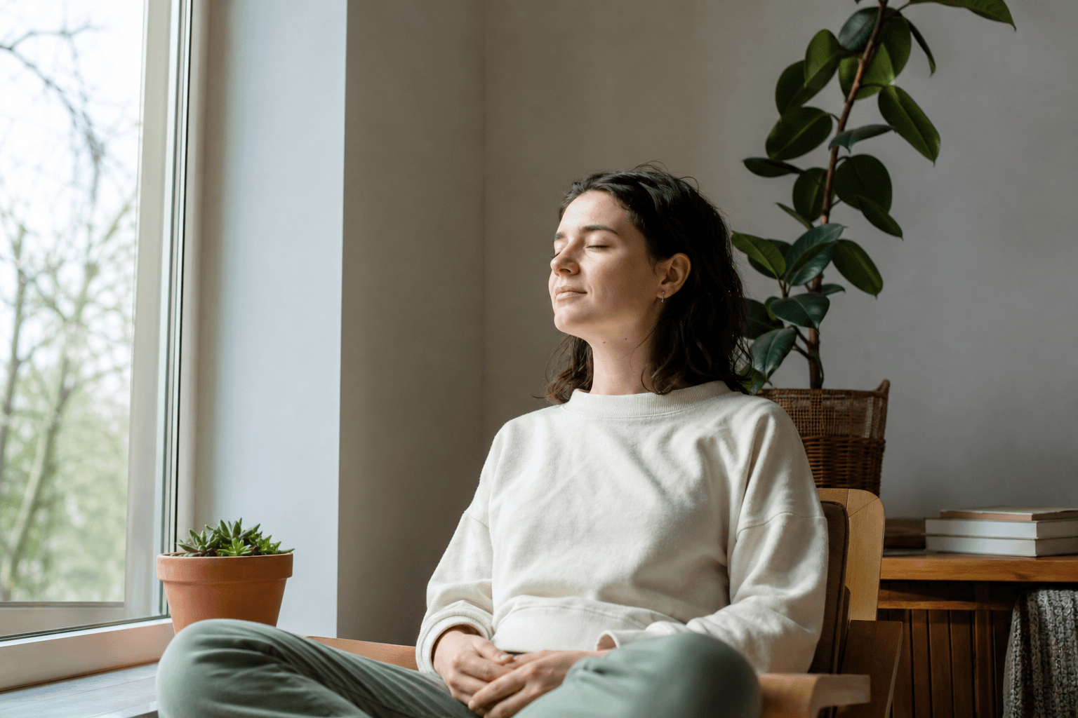 A person sitting calmly with eyes closed, breathing slowly in a quiet, light-filled room
