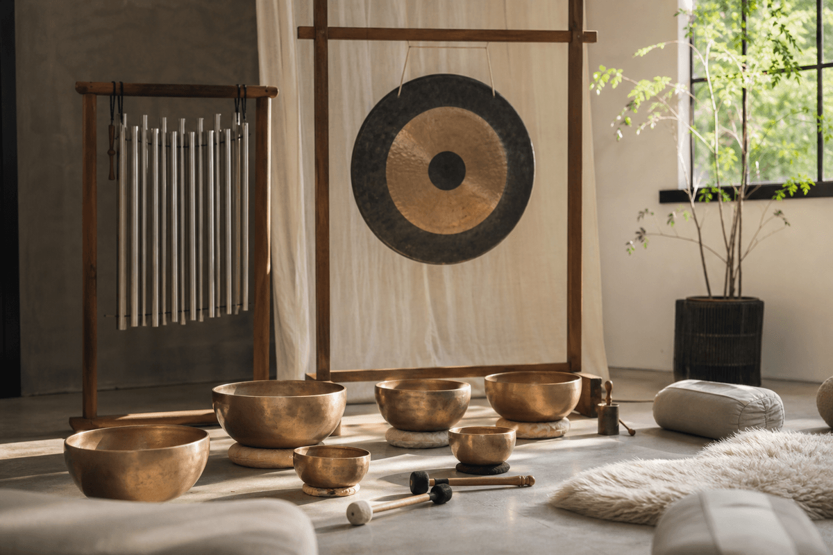 Singing bowls, chimes, and a gong arranged on a calm studio floor with soft light and a few cushions