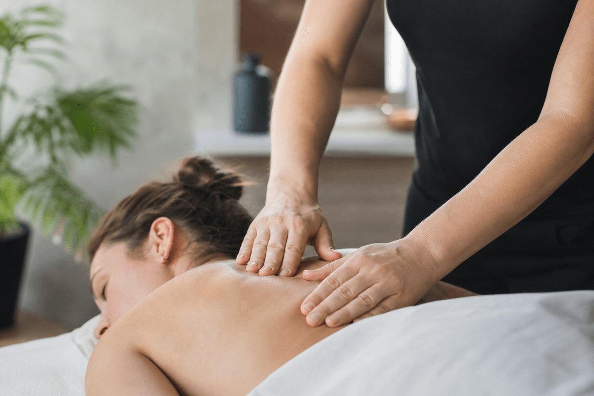 A massage therapist's hands resting flat on a client's upper back with light, even pressure in a calm treatment room