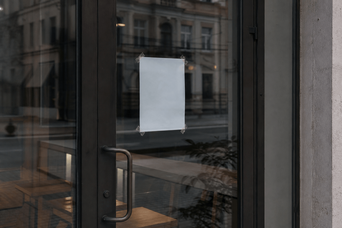 A closed glass storefront door with a paper notice taped inside, seen from the street