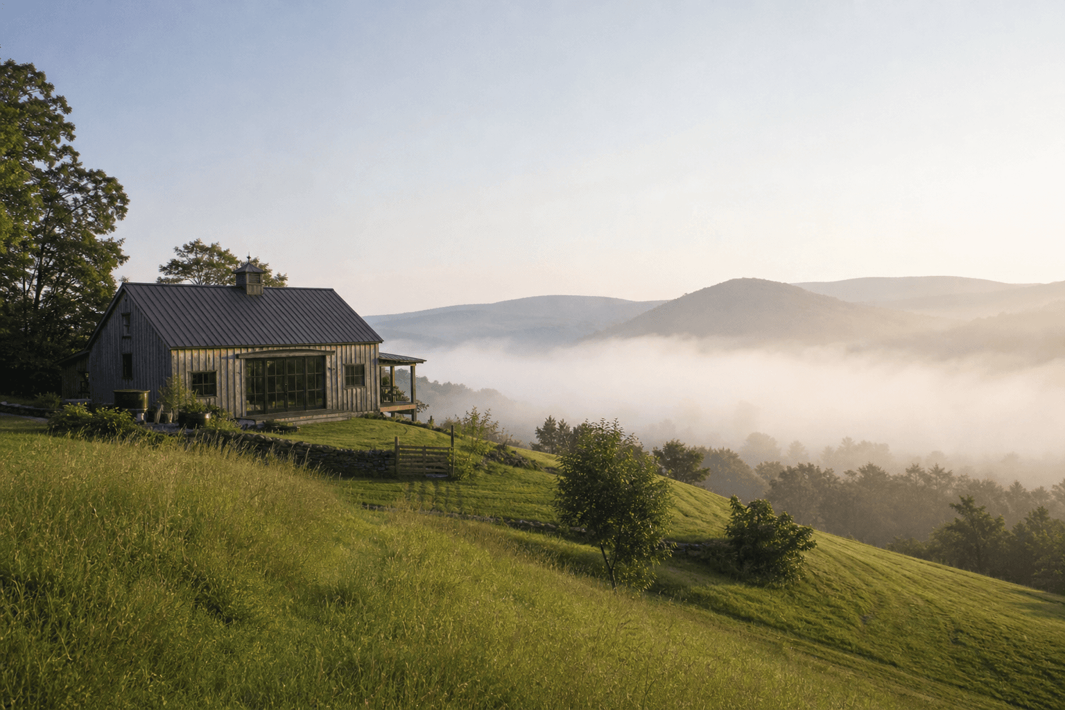 A converted barn retreat on a green hillside in the Catskills with morning mist rising off the valley