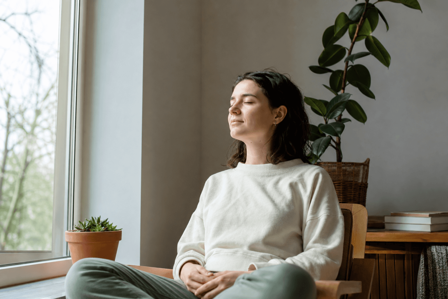 A person sitting calmly with eyes closed, breathing slowly in a quiet, light-filled room