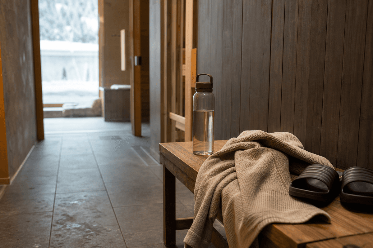 A wooden bench beside a locker room with a towel, water bottle and sandals