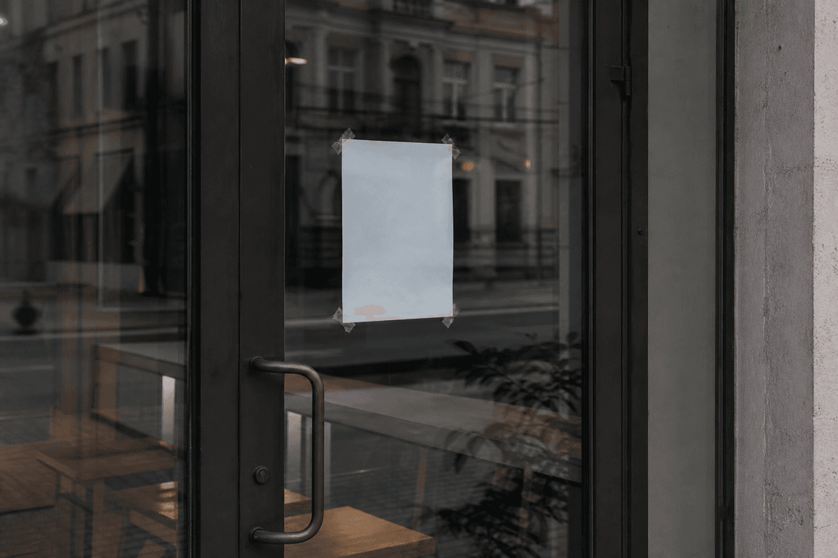 A closed glass storefront door with a paper notice taped inside, seen from the street
