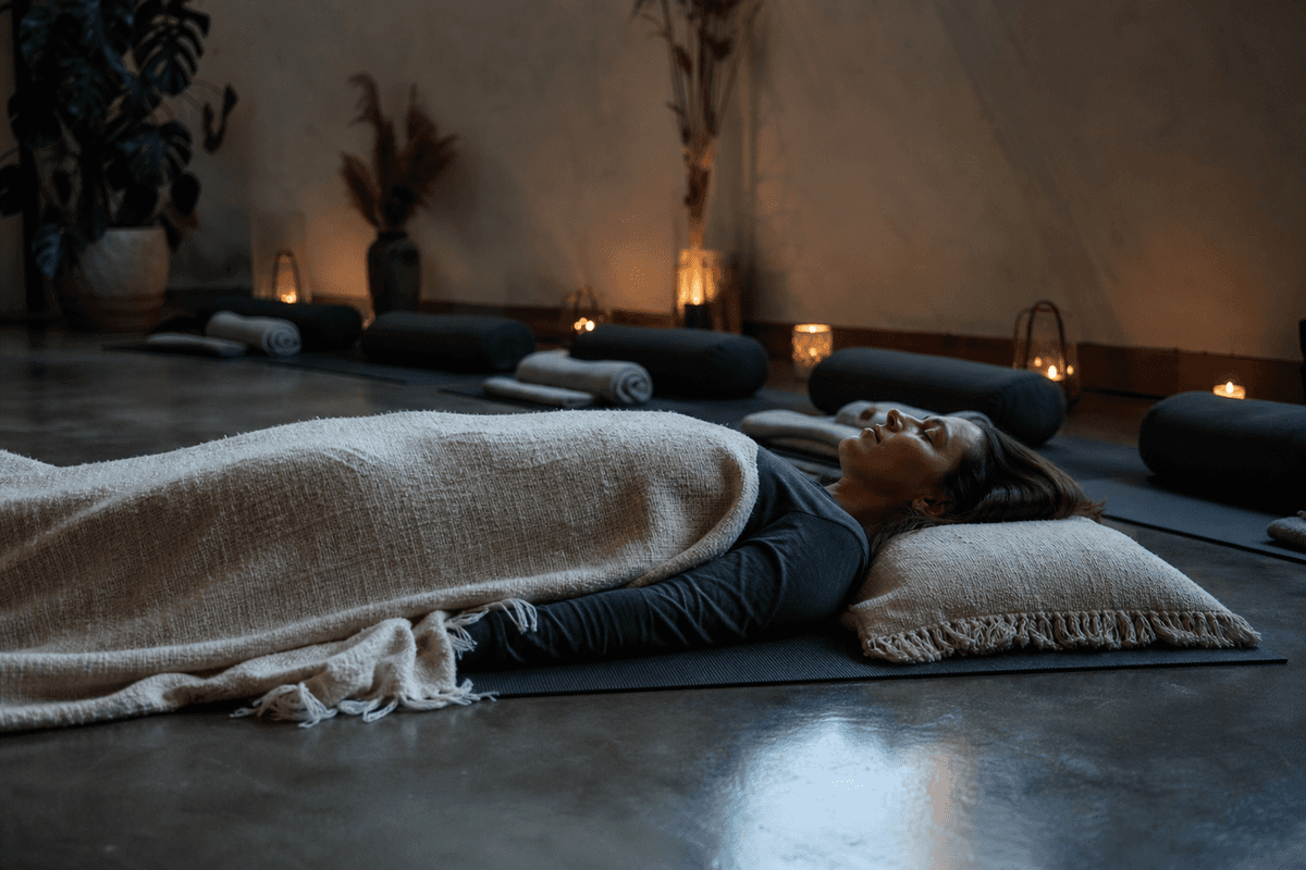 A calm dim studio with a person lying on a mat under a blanket during a breathwork session